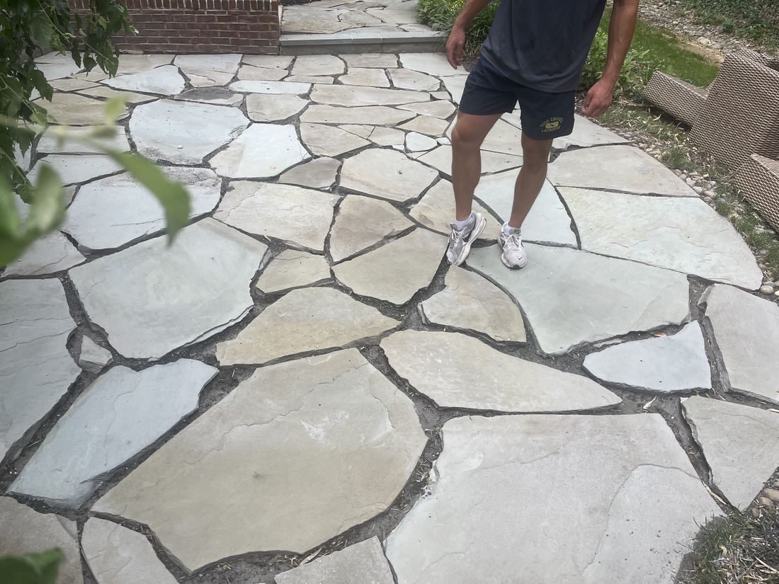 Flagstone patio before cleaning, with weeds and dirt in the joints